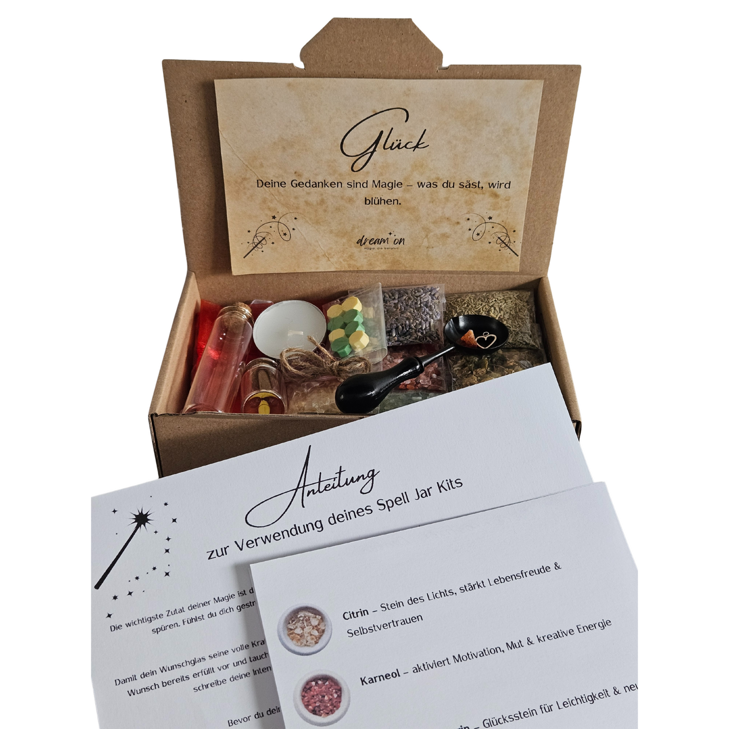 Geöffnete Geschenkbox des DIY-Kreativsets Glück von DreamOn, gefüllt mit Naturmaterialien und Zubehör. Im Vordergrund liegt eine gedruckte Anleitung zur Verwendung des Sets mit Beschreibungen zu Citrin, Karneol und Aventurin.