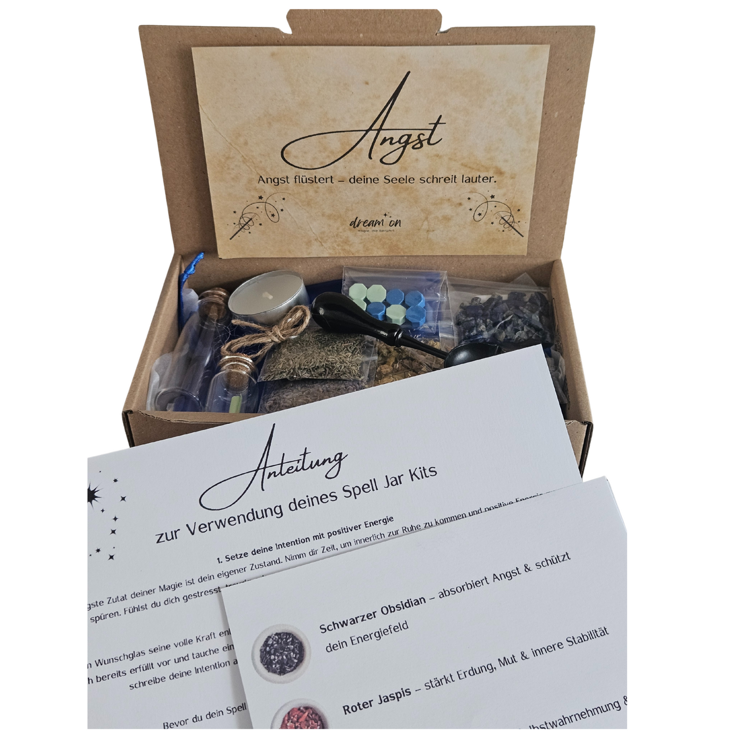 Geöffnete Geschenkbox des DIY-Kreativsets Angst loslassen von DreamOn, gefüllt mit Naturmaterialien und Zubehör. Im Vordergrund liegt eine gedruckte Anleitung zur Verwendung des Sets mit Beschreibungen zu Schwarzem Obsidian, Rotem Jaspis und Lapislazuli.
