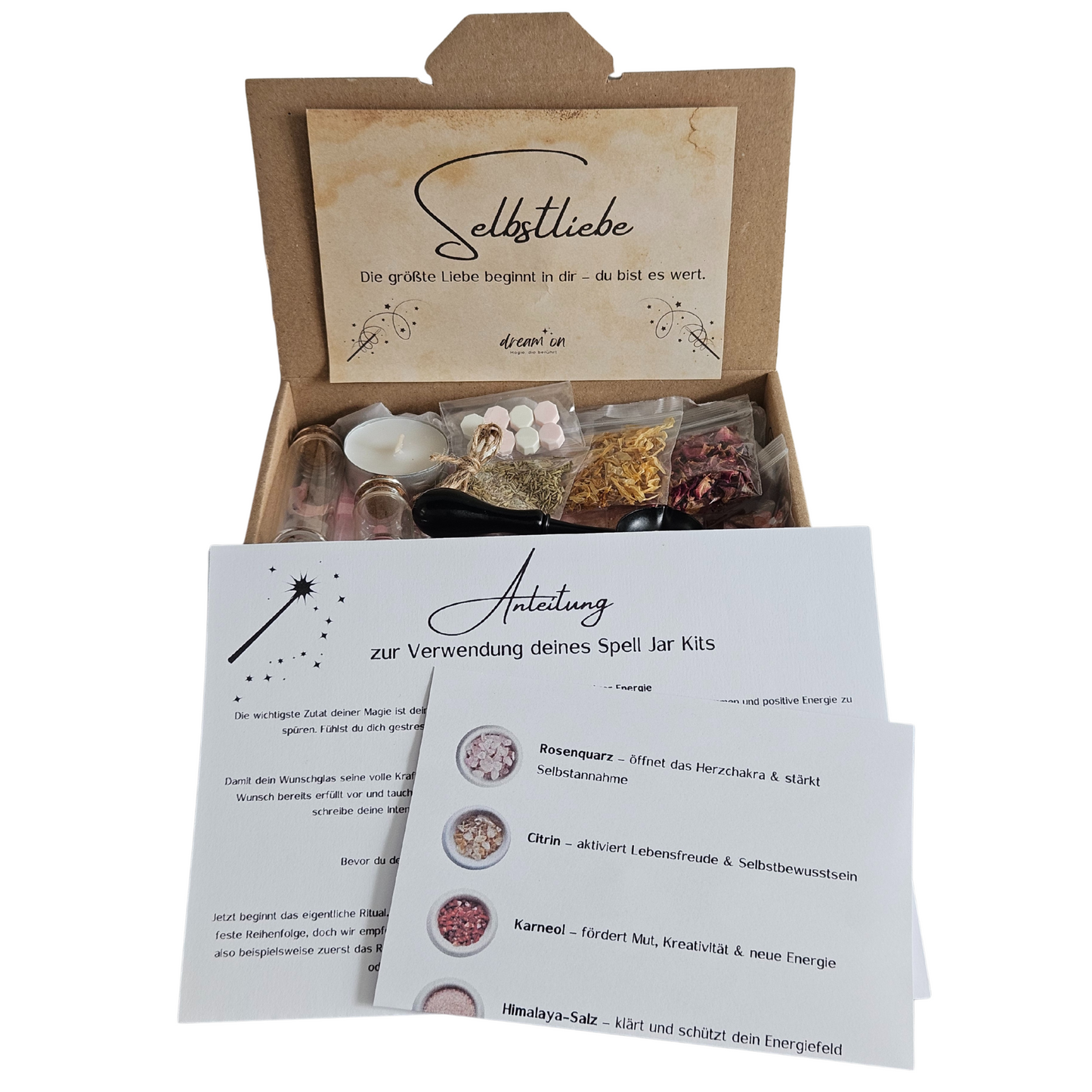 Geöffnete Geschenkbox des DIY-Kreativsets Selbstliebe von DreamOn, gefüllt mit Naturmaterialien und Zubehör. Im Vordergrund liegt eine gedruckte Anleitung zur Verwendung des Sets mit Beschreibungen zu Rosenquarz, Citrin und Karneol.