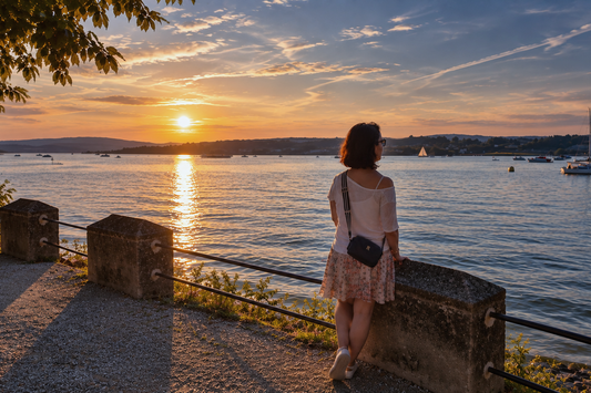 Frau blickt bei Sonnenuntergang über einen See – Sinnbild für die Balance zwischen Magie und echtem Leben.