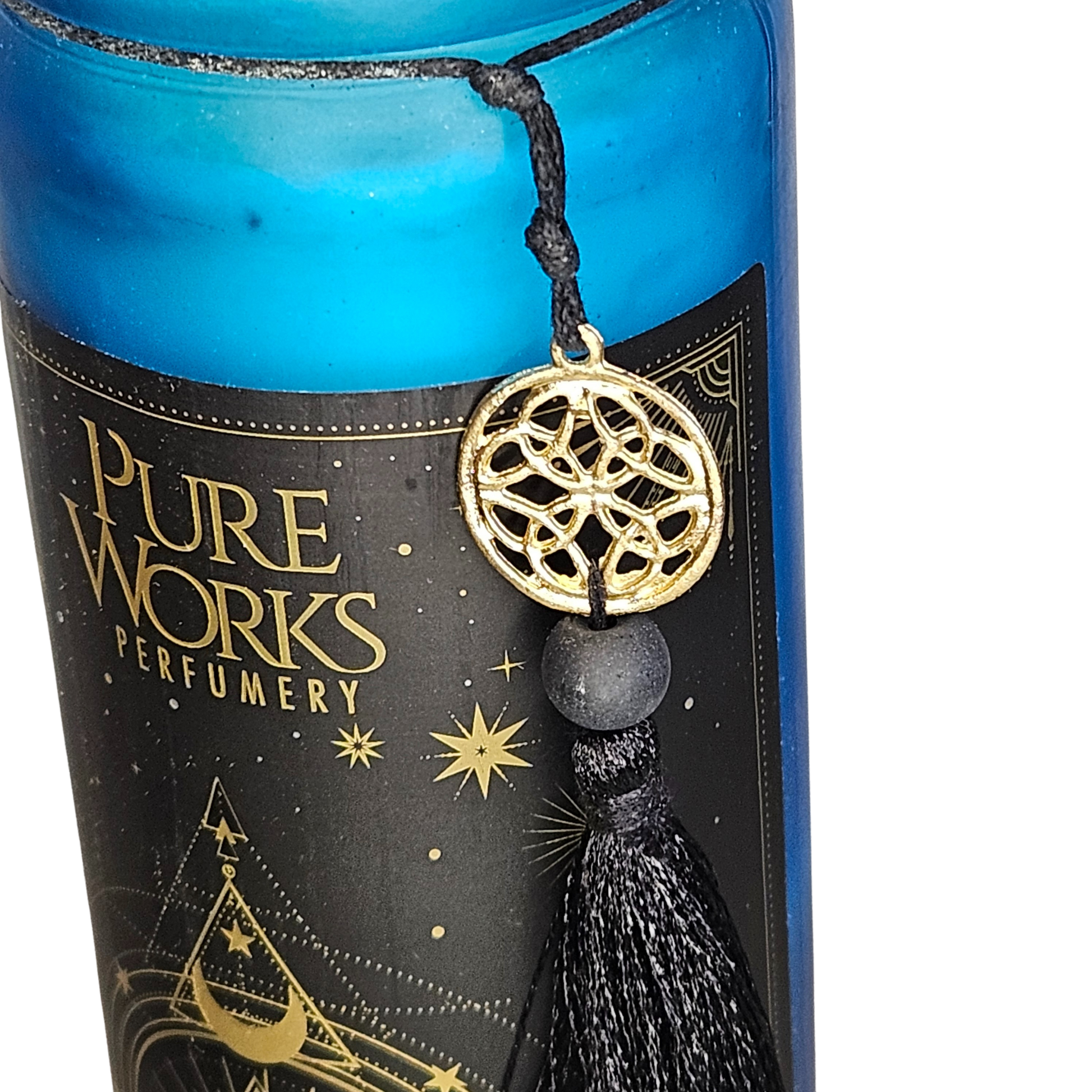Detailansicht der grünen Glas-Duftkerze mit der goldenen Linienverzierung, dem PureWorks-Logo und der befestigten schwarzen Stoffquaste.