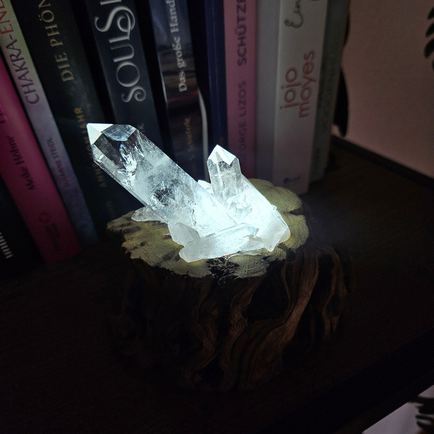 Leuchtender Bergkristall auf handgefertigtem Holzsockel bei Dunkelheit
