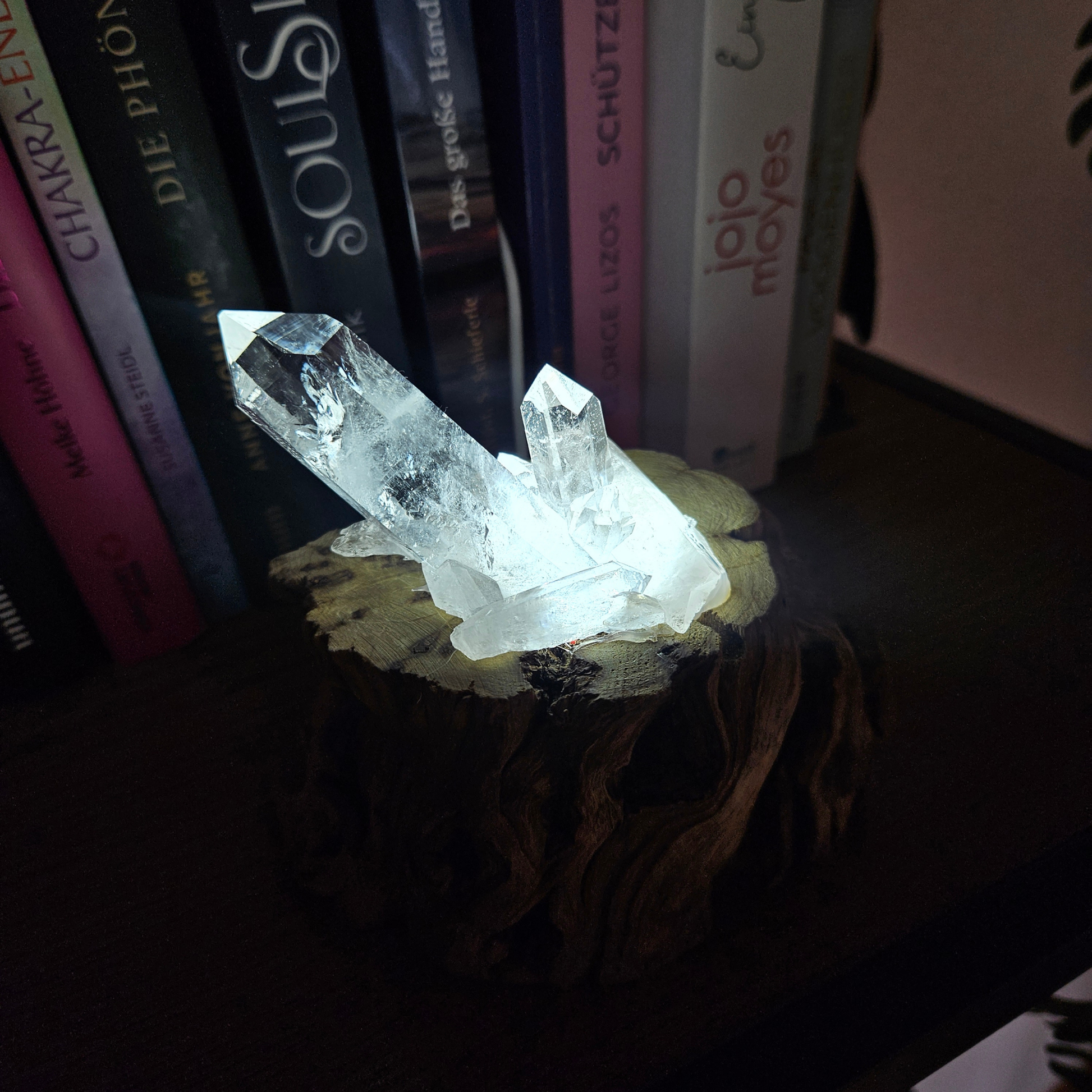 Leuchtender Bergkristall auf handgefertigtem Holzsockel bei Dunkelheit