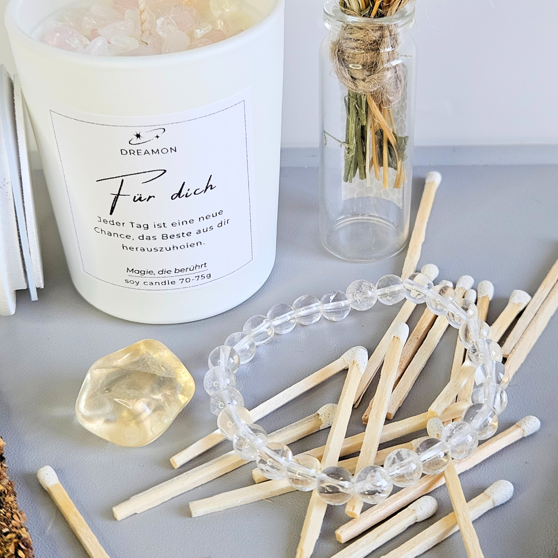 Nahaufnahme Geschenkset „Für dich“ – weiße Duftkerze mit Edelsteinen, Glasflasche mit Streichhölzern, Mondstein-Armband, Mondstein und Trockenblumen.