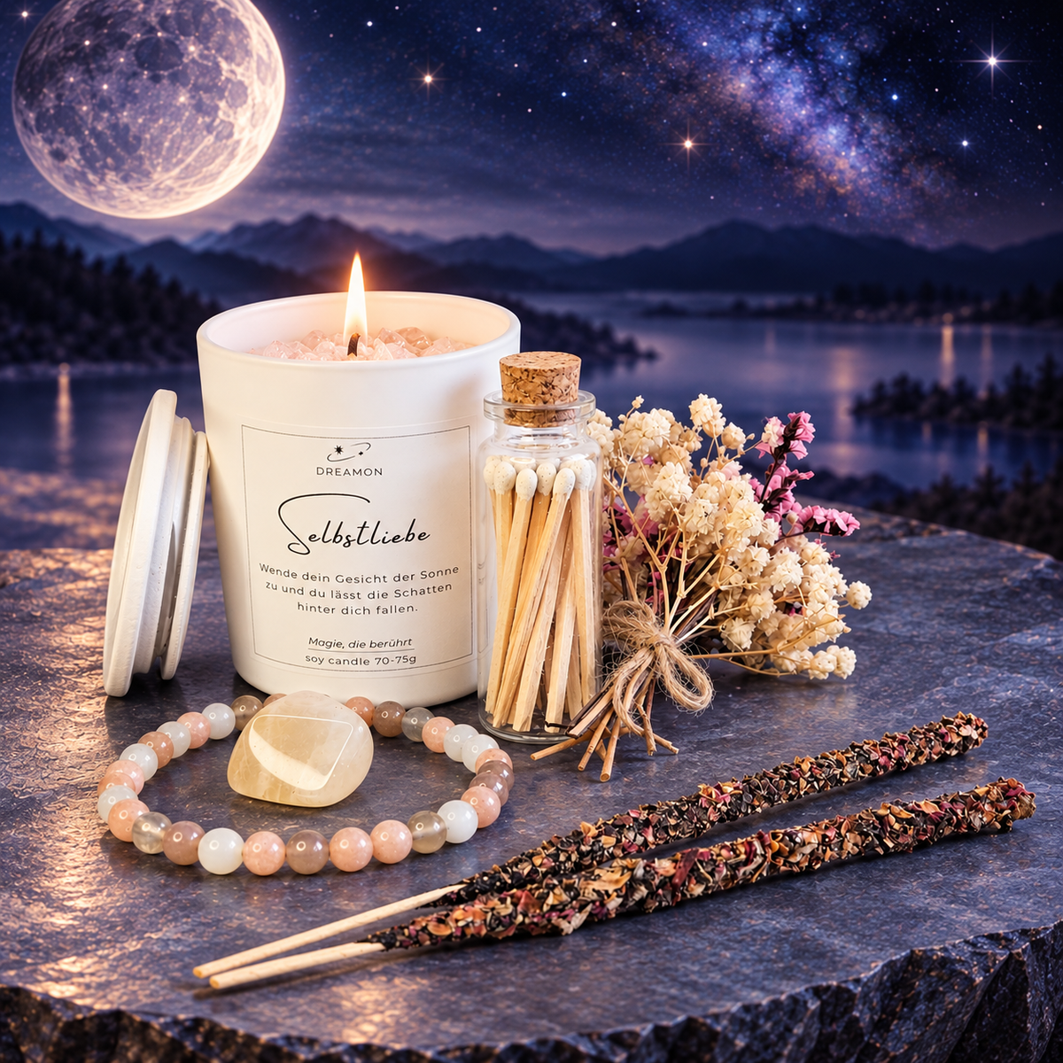 DreamOn Geschenkset Selbstliebe mit Duftkerze, Edelstein-Armband, Trommelstein, Räucherstäbchen und Trockenblumen auf Steinunterlage vor Sternenhimmel.