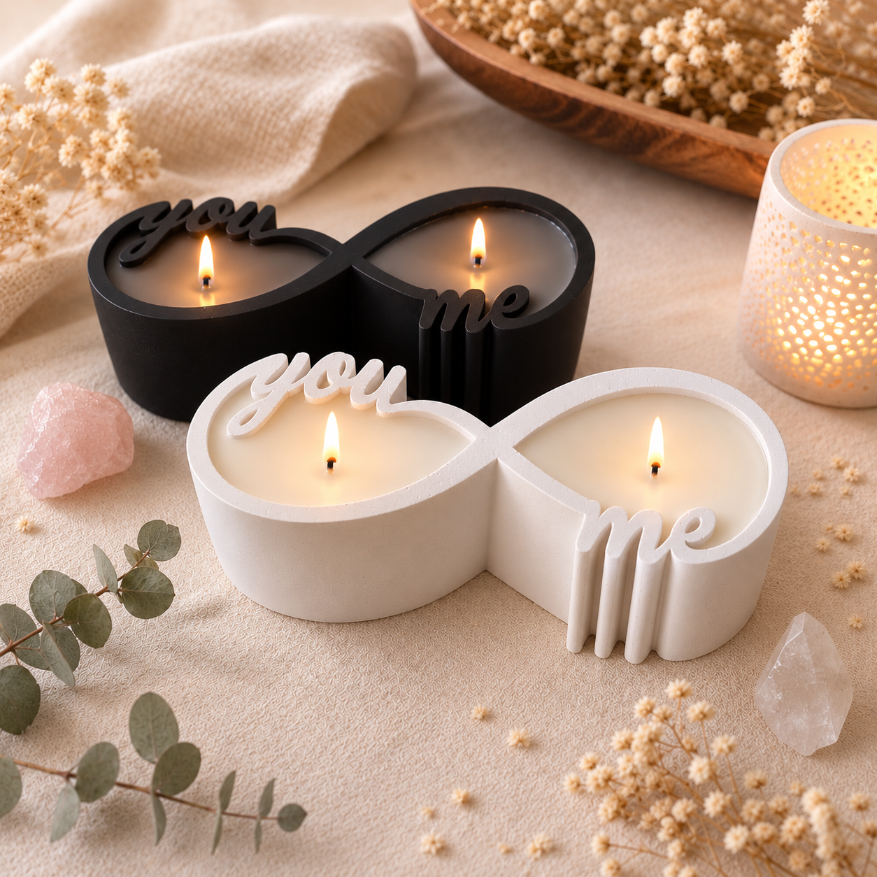 Ästhetische Produktfotografie der brennenden schwarzen und weissen Infinity-Kerzen auf einem beigen Leinentuch, umgeben von Trockenblumen und Heilsteinen.