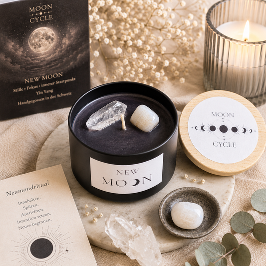 Geöffnete schwarze Duftkerze „New Moon“ mit dunklem Wachs und zwei eingebetteten Natursteinen auf einer hellen Marmorplatte, umgeben von Deko-Elementen und einer brennenden Kerze im Hintergrund.