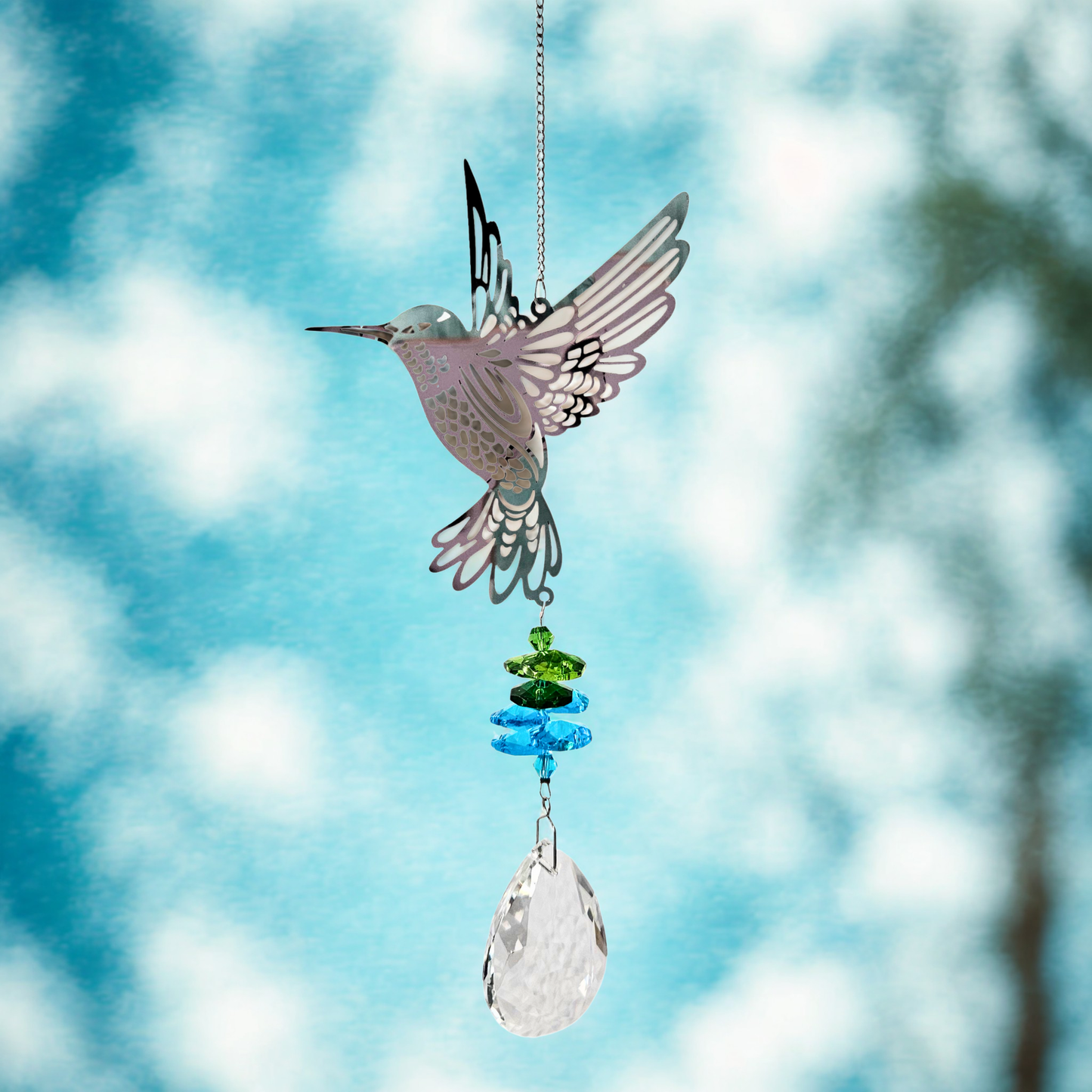 Kolibri-Sonnenfänger aus Metall mit farbigen Kristallen, hängend vor blauem Himmel mit weichen Wolken.