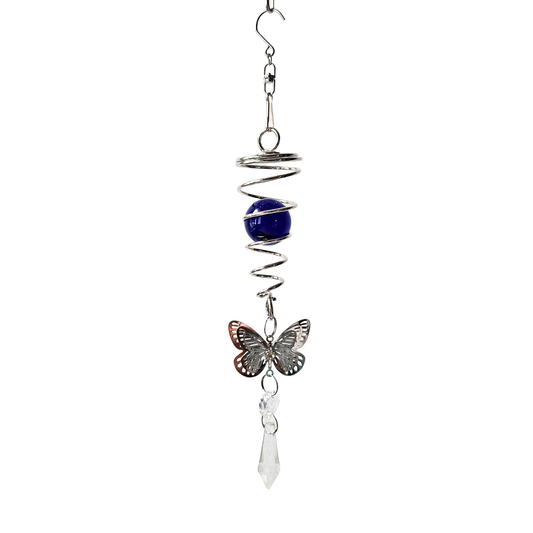 Sonnenfänger aus Edelstahl mit blauer Kristallkugel in einer spiralförmigen Halterung, filigranem Metallschmetterling und klarem Kristallprisma, vor weißem Hintergrund