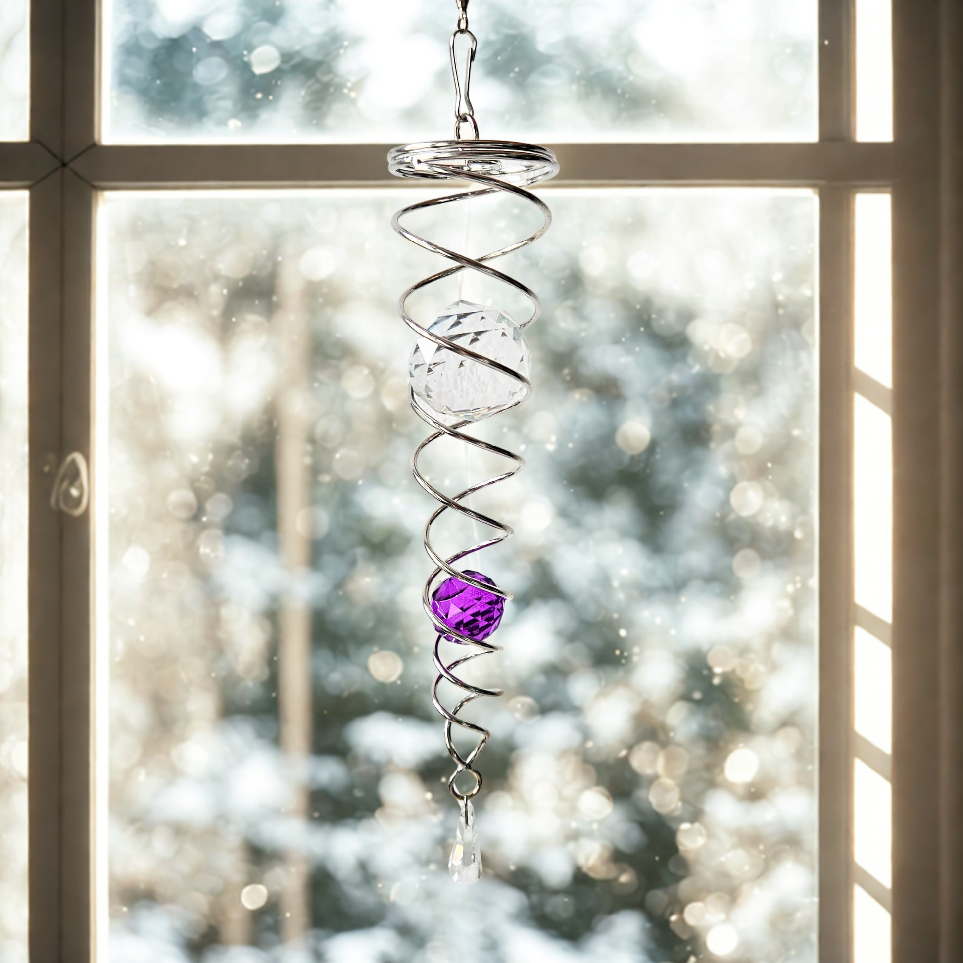 Windrotierende Edelstahl-Spirale mit Kristallkugeln, hängend vor einem Fenster im winterlichen Sonnenlicht.