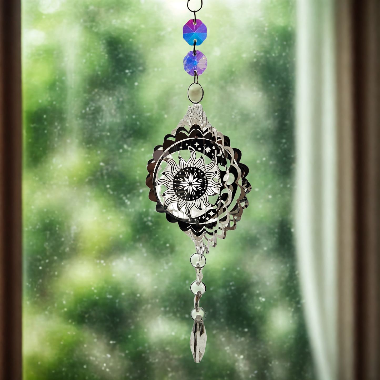 Metall-Suncatcher Windspiel mit Sonne-und-Mond-Motiv und Kristallanhänger, hängend vor einem Fenster.