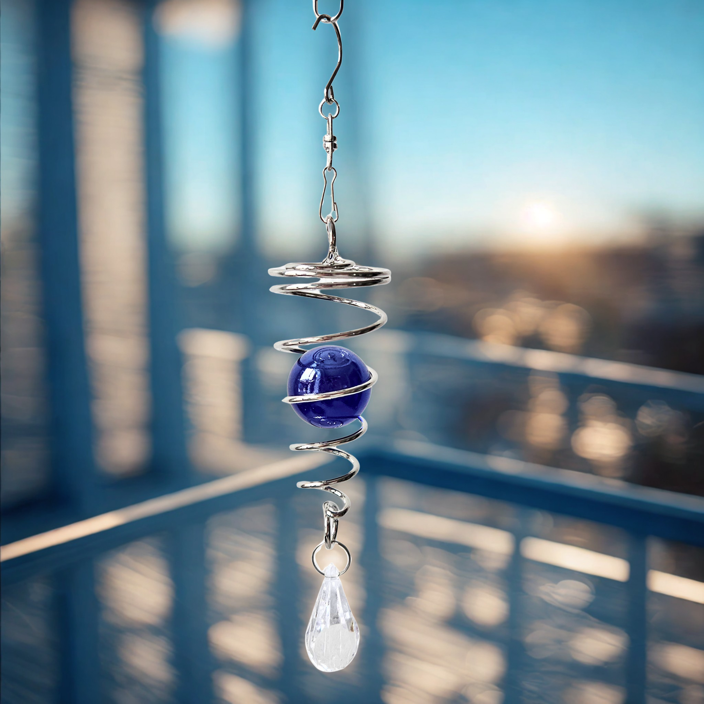 Kleiner Sonnenfänger mit Metallspirale und Kristallkugel, hängend auf einem Balkon im Abendlicht.
