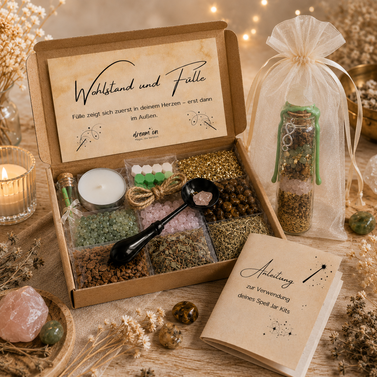 Geöffnete Geschenkbox des DIY-Kreativsets Wohlstand und Fülle von DreamOn mit Naturmaterialien, Kristallen, Goldflocken und Zubehör zum Versiegeln. Rechts steht ein fertig gestaltetes Wunschglas mit grünem Wachssiegel im hellen Organzasäckchen, im Vordergrund liegt das Anleitungsheft.