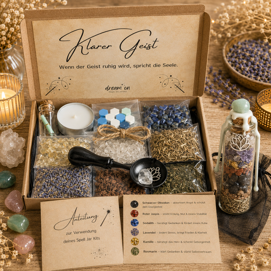 Geöffnete Geschenkbox des DIY-Kreativsets Klarer Geist von DreamOn mit Bergkristall, Lapislazuli, Citrin und getrockneten Kräutern. Rechts steht das fertig geschichtete Wunschglas mit hellgrünem Wachssiegel, Lotus-Anhänger und Rotem Jaspis vor einem schwarzen Organzasäckchen, im Vordergrund liegt die gedruckte Anleitung mit Zubehör.