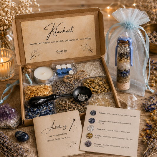 Geöffnete Geschenkbox des DIY-Kreativsets Klarheit von DreamOn mit Sodalith, Lapislazuli, Bergkristall und Kräutern. Rechts steht ein fertig gestaltetes Wunschglas mit hellblauem Wachssiegel in einem hellblauen Organzasäckchen, im Vordergrund liegt die gedruckte Anleitung.