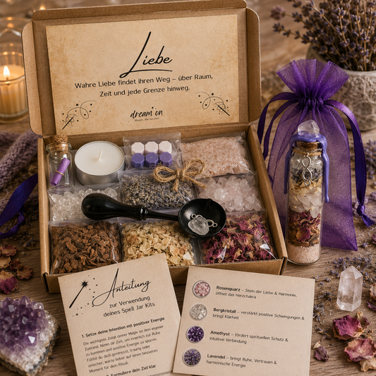 Geöffnete Geschenkbox des DIY-Kreativsets Liebe von DreamOn mit Rosenquarz, Bergkristall, Amethyst, Lavendel und Rosenblättern. Rechts steht ein fertig geschichtetes Wunschglas mit violettem Wachssiegel im Organzasäckchen, davor liegt die gedruckte Anleitung.