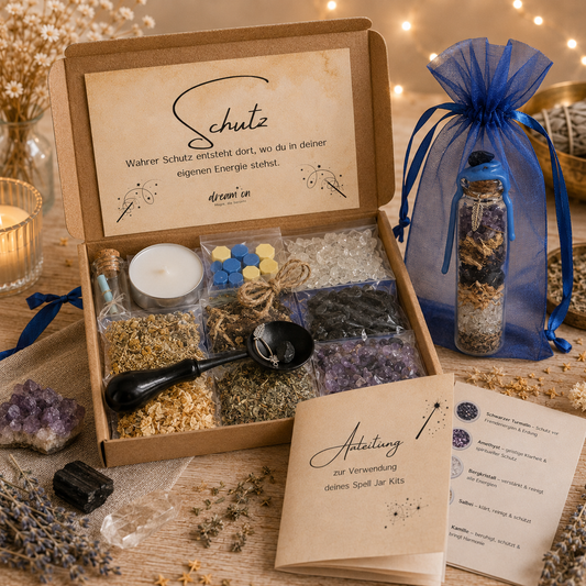 Geöffnete Geschenkbox des DIY-Kreativsets Schutz von DreamOn, gefüllt mit Schwarzem Turmalin, Amethyst, Bergkristall und Kräutern. Daneben steht das fertige, blau versiegelte Wunschglas im blauen Organzasäckchen, umgeben von der gedruckten Anleitung.
