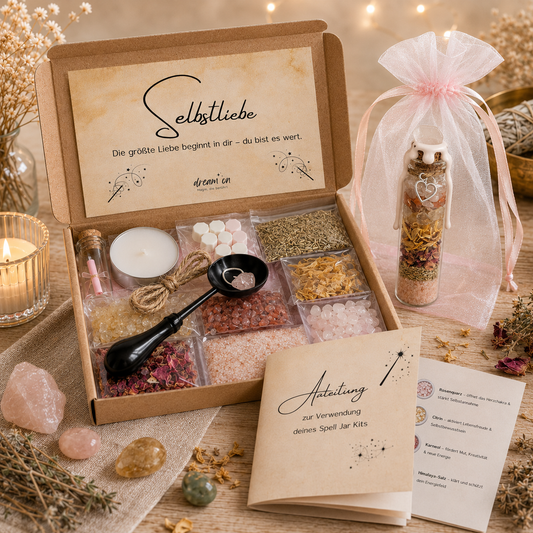 Geöffnete Geschenkbox des DIY-Kreativsets Selbstliebe von DreamOn, gefüllt mit Rosenquarz, Citrin, Karneol, Himalaya-Salz und Kräutern. Daneben steht ein fertig geschichtetes Wunschglas mit weißem Wachssiegel in einem rosa Organzasäckchen, umgeben von Deko und Anleitung.