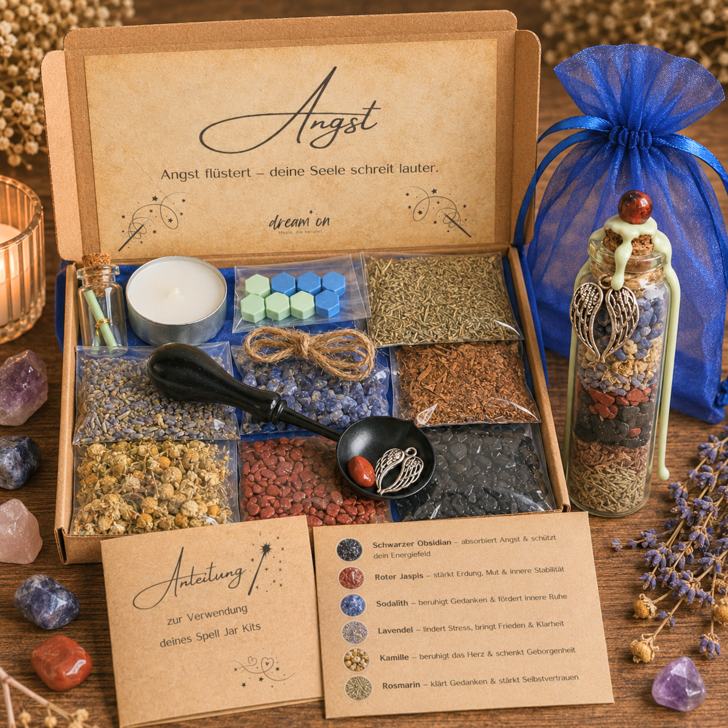 Geöffnete Geschenkbox des DIY-Kreativsets Vertrauen von DreamOn mit der Aufschrift Angst im Deckel, gefüllt mit Schwarzem Obsidian, Rotem Jaspis, Sodalith und Kräutern. Rechts steht das fertig gestaltete Wunschglas mit hellgrünem Wachssiegel und Flügel-Anhänger vor einem blauen Organzasäckchen.