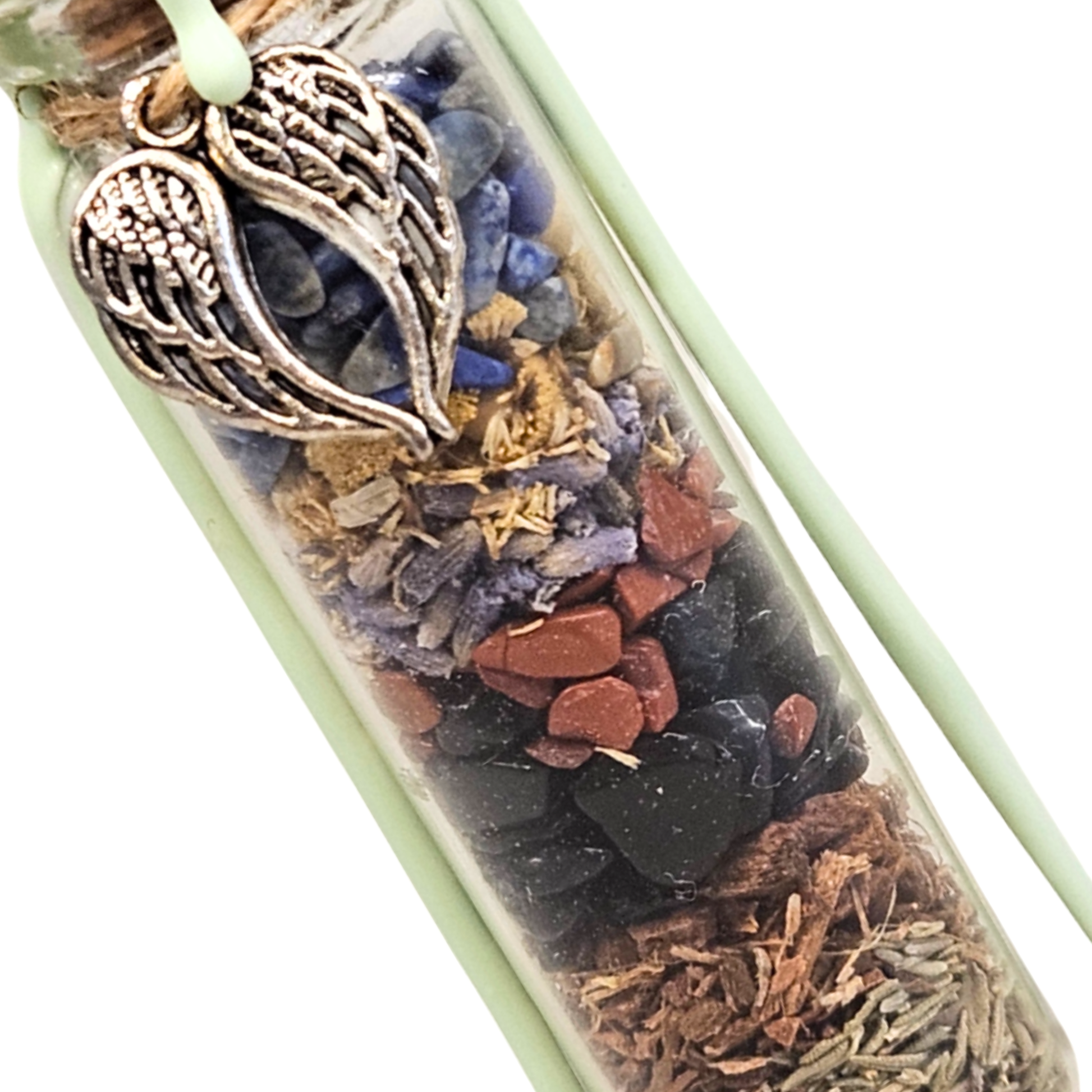 Detailaufnahme eines Deko-Glasfläschchens mit präzisen Schichten aus tiefschwarzem Obsidian, ziegelrotem Jaspis, dunkelblauem Lapislazuli sowie getrockneter Eichenrinde, Thymian und Lavendel.
